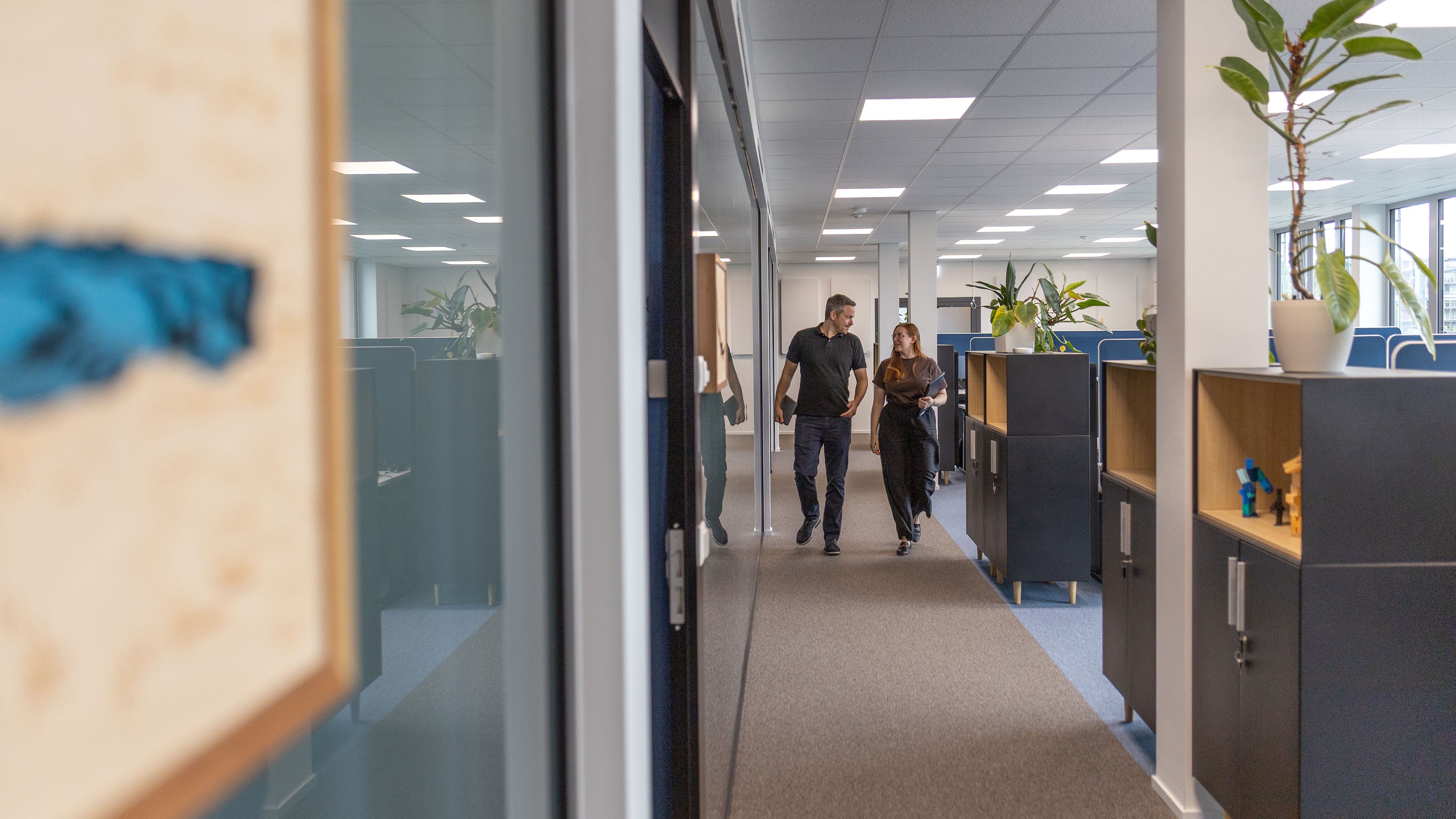 Zwei Mitarbeitende gehen durch den Büroflur und unterhalten sich