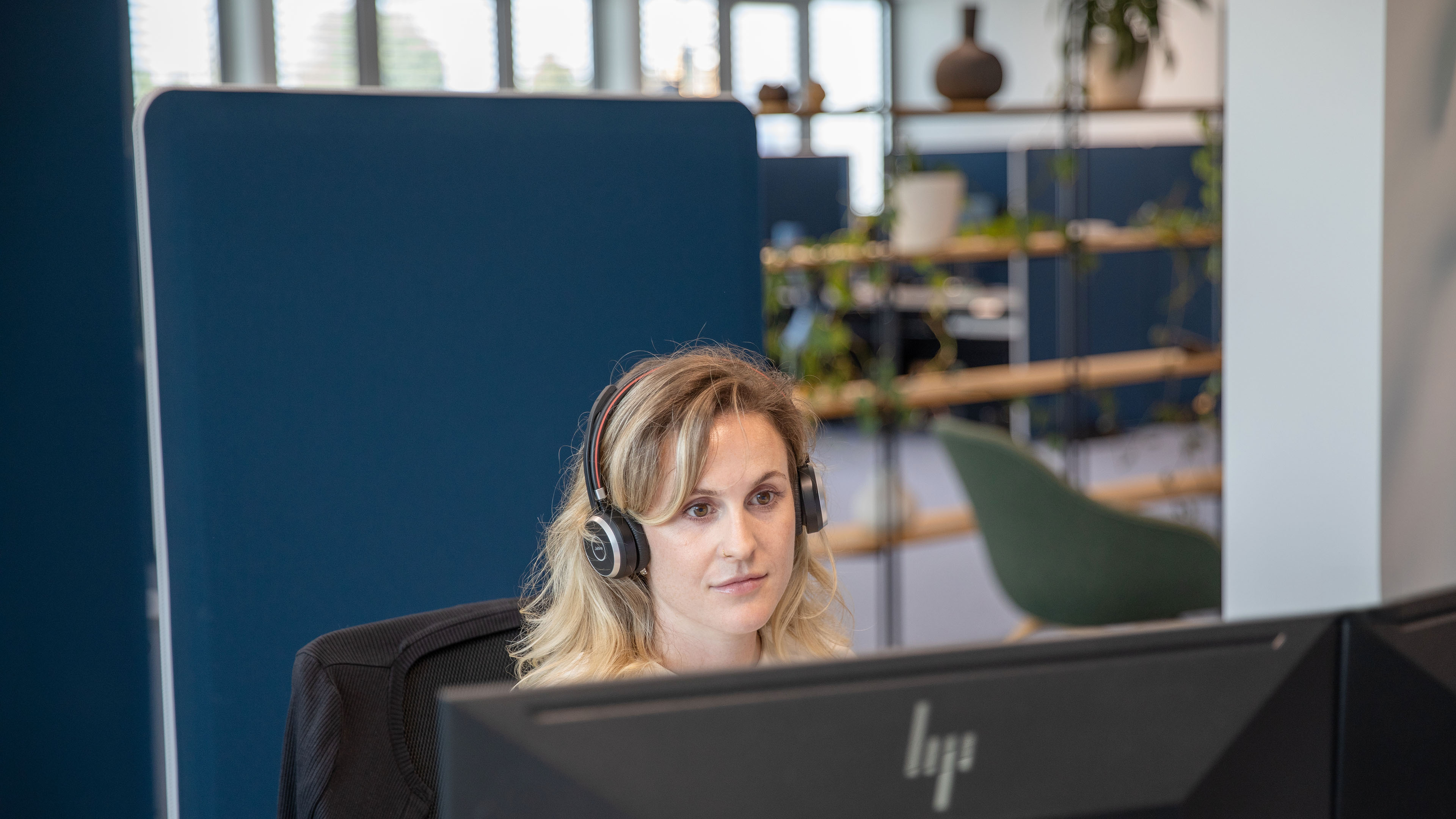 Eine Mitarbeiterin trägt ein Headset und arbeitet konzentriert am Computer