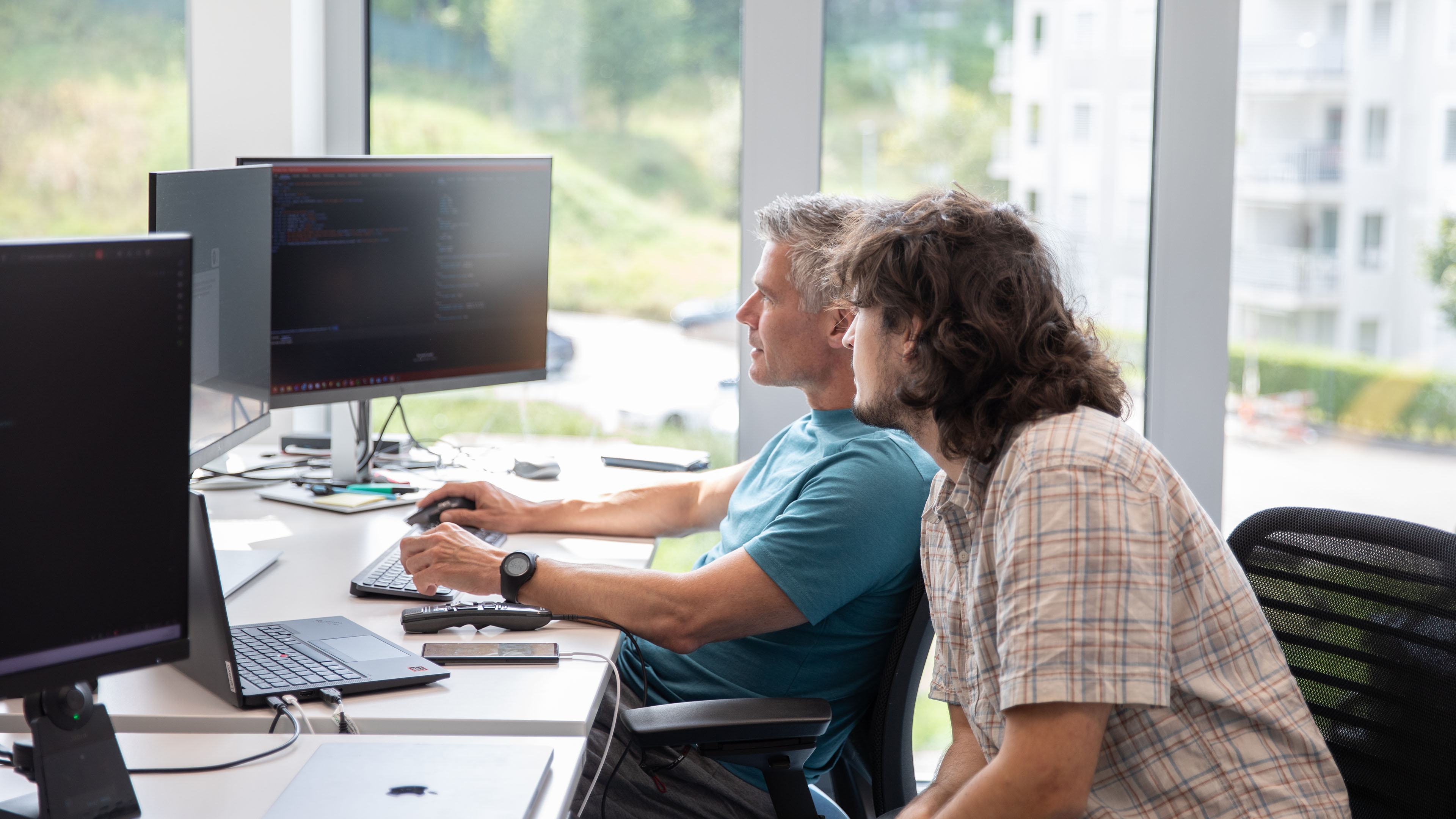 Zwei Mitarbeitende sitzen am Arbeitsplatz vor zwei Bildschirmen und arbeiten gemeinsam an einer Softwarelösung