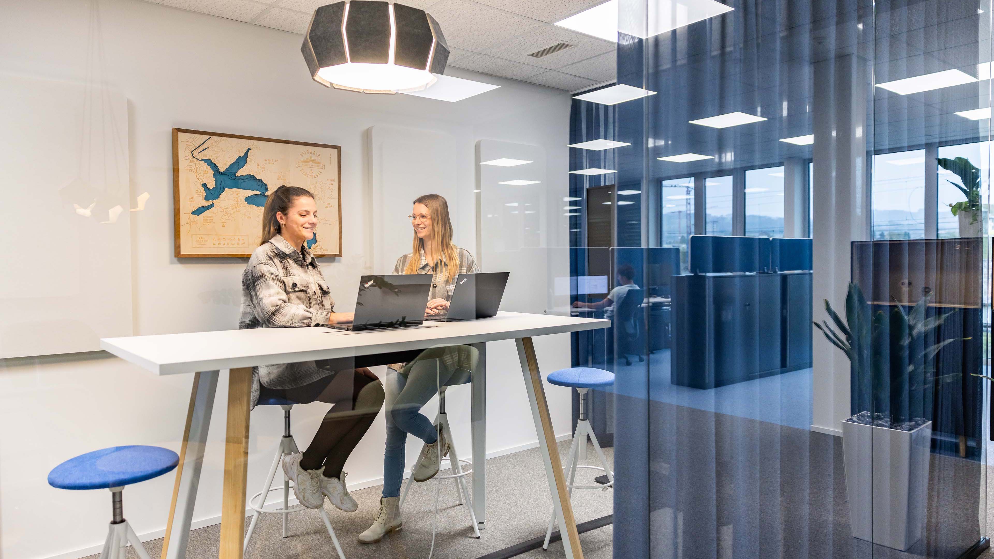 Zwei Mitarbeitende der Voicepoint AG sitzen mit Laptops an einem hohen Tisch und tauschen sich aus.