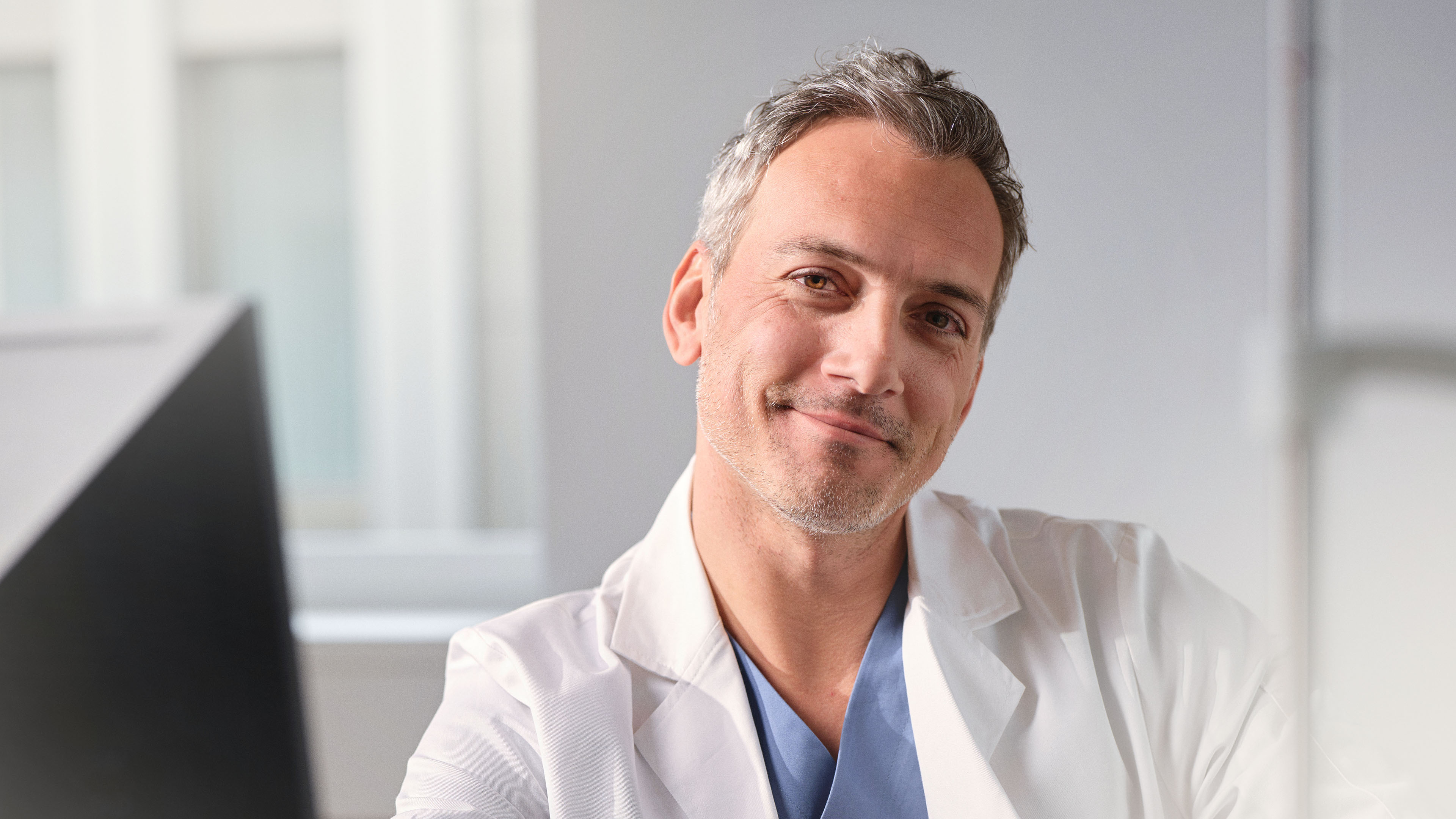 Un médecin en blouse blanche sourit aimablement à la caméra.