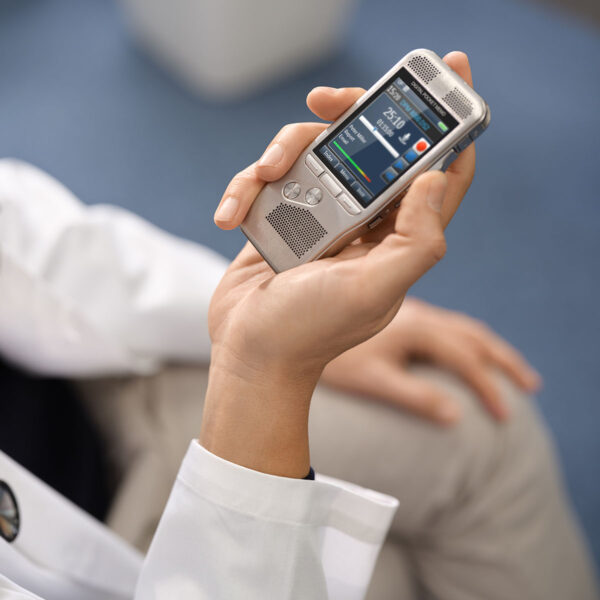 Un médecin en blouse blanche dicte, assis, à l'aide d'un dictaphone Philips Digital Pocket Memo 8000