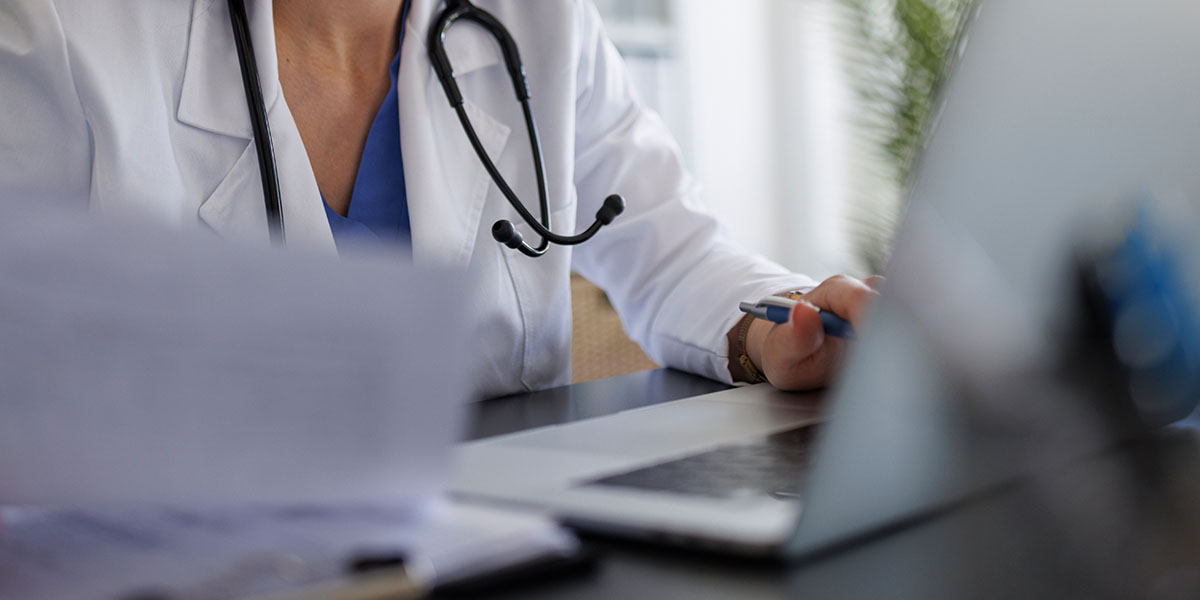Ärztin sitz an Schreibtisch und dokumentiert ein Patientengespräch.