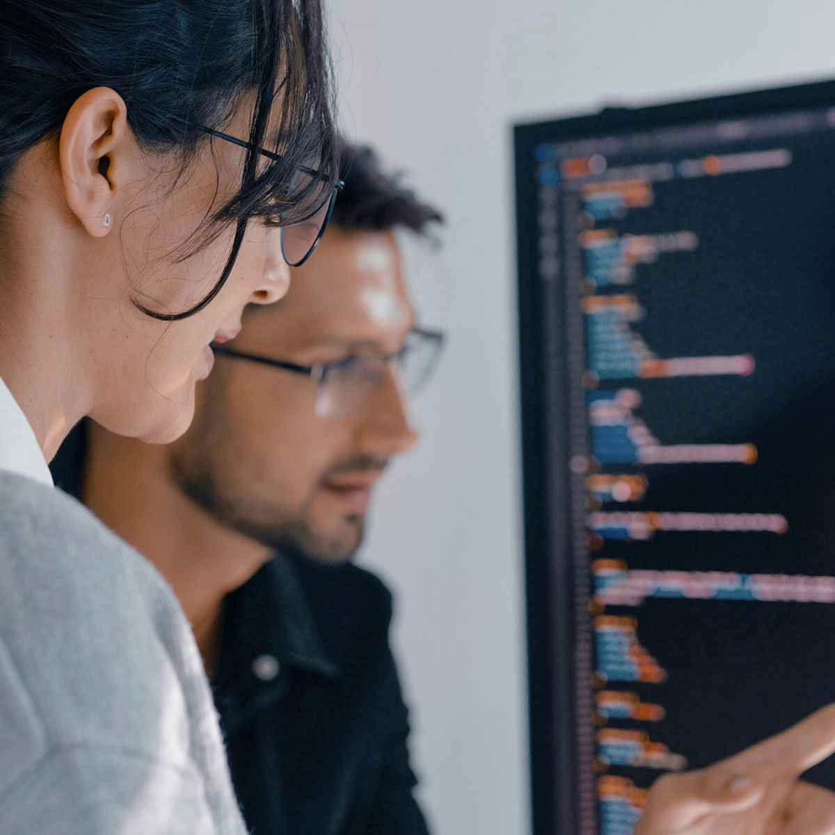 Zwei Personen blicken konzentriert auf einen Bildschirm, auf dem Code zu sehen ist.