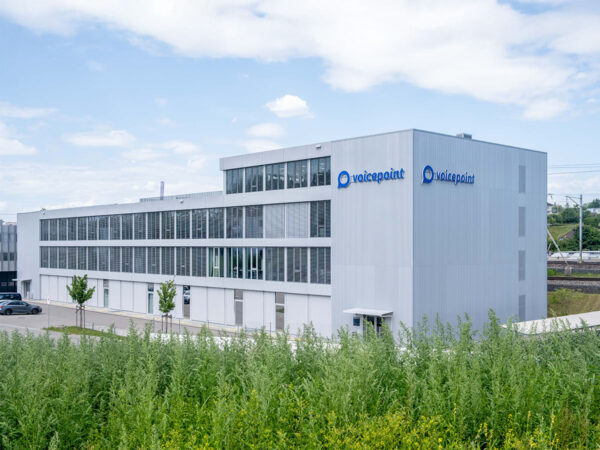 Graues Firmengebäude der Voicepoint AG mit grossen Fenstern und einer grünen Wiese im Vordergrund.