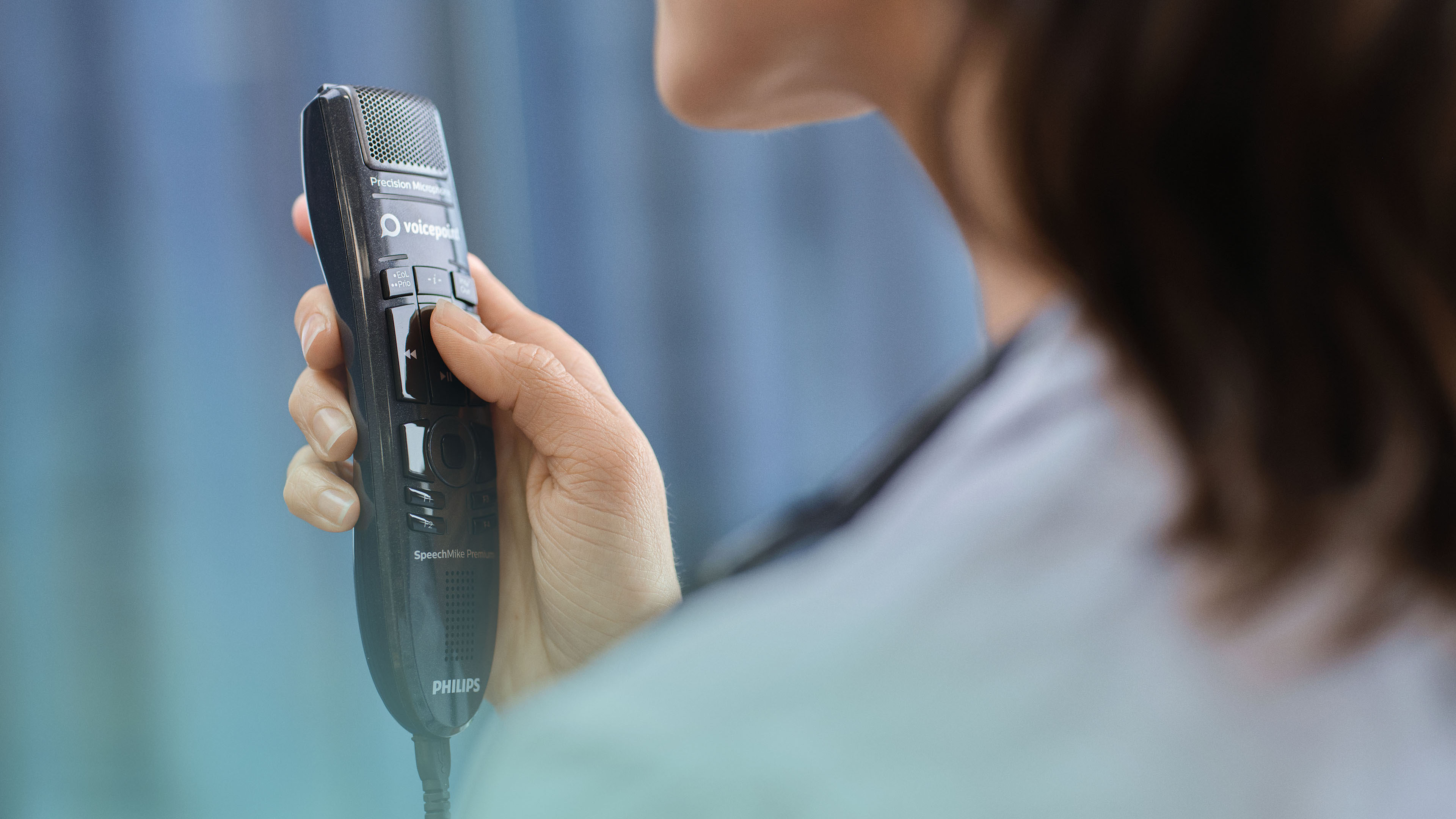 Gros plan d'une médecin dictant avec un microphone. Des dégradés de couleur turquoise sont visibles sur les bords de l'image.