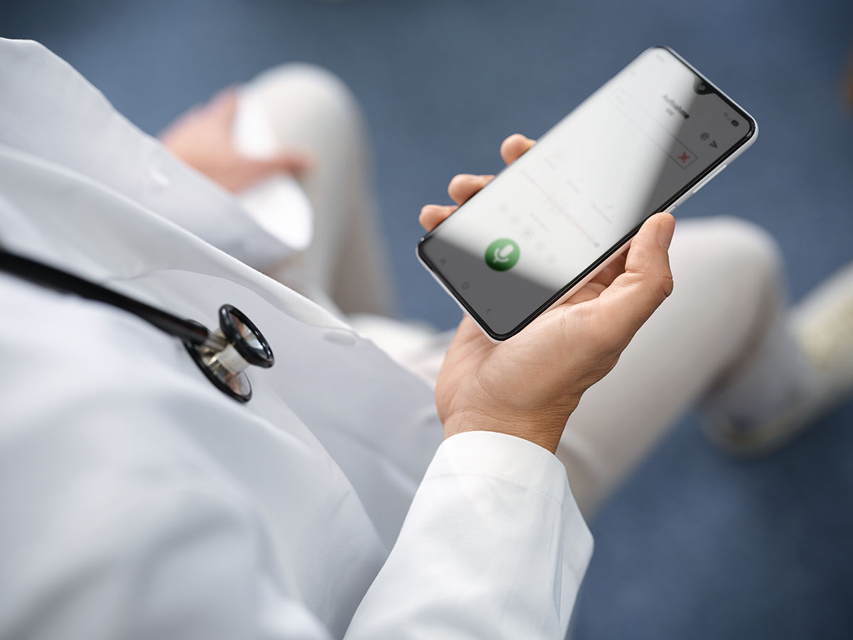 Arzt im weissen Kittel hält ein Smartphone in der Hand und diktiert mit der Voicepoint Xenon App.